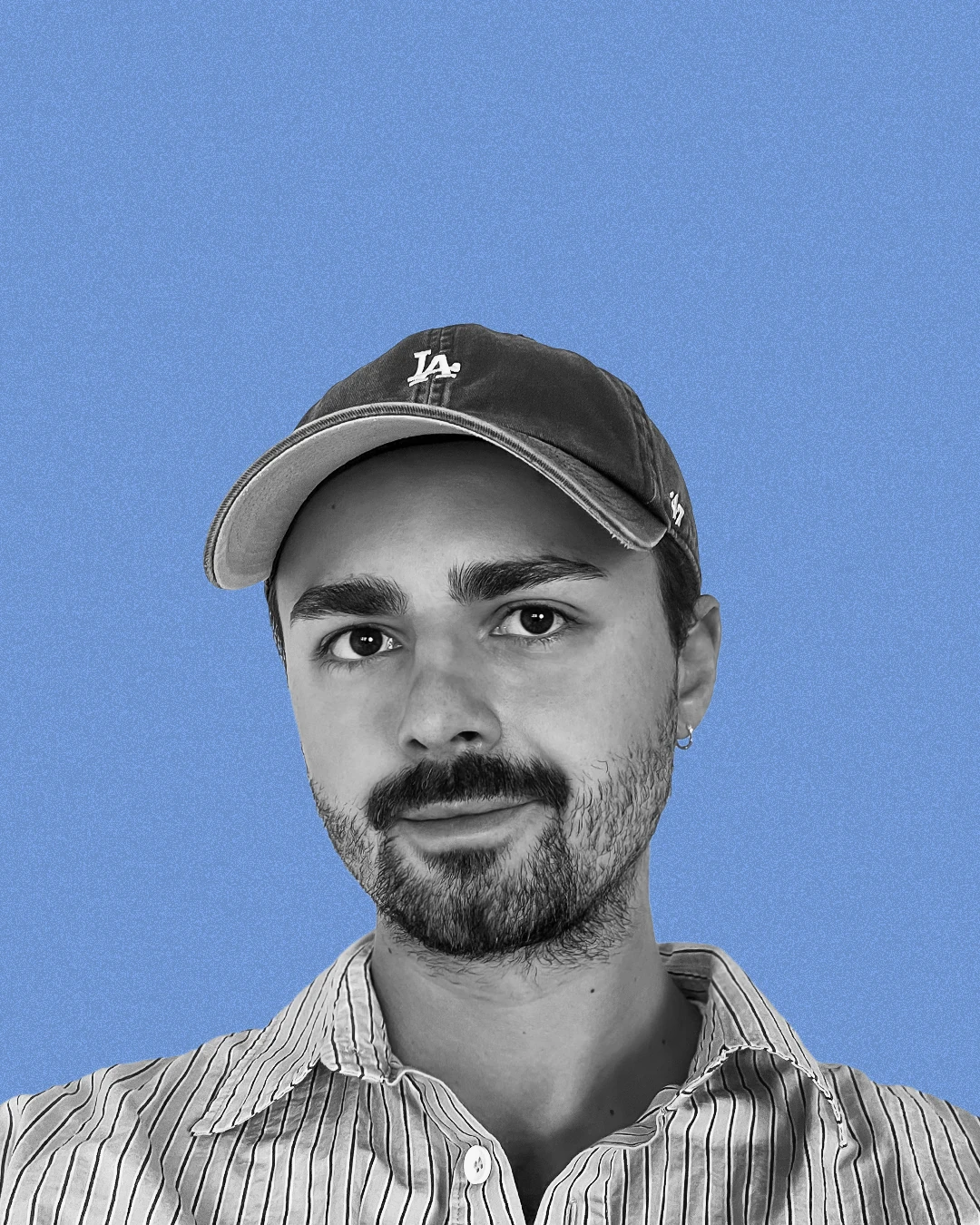 Portrait of Dominik Rudnicki in a cap and striped shirt against a blue background