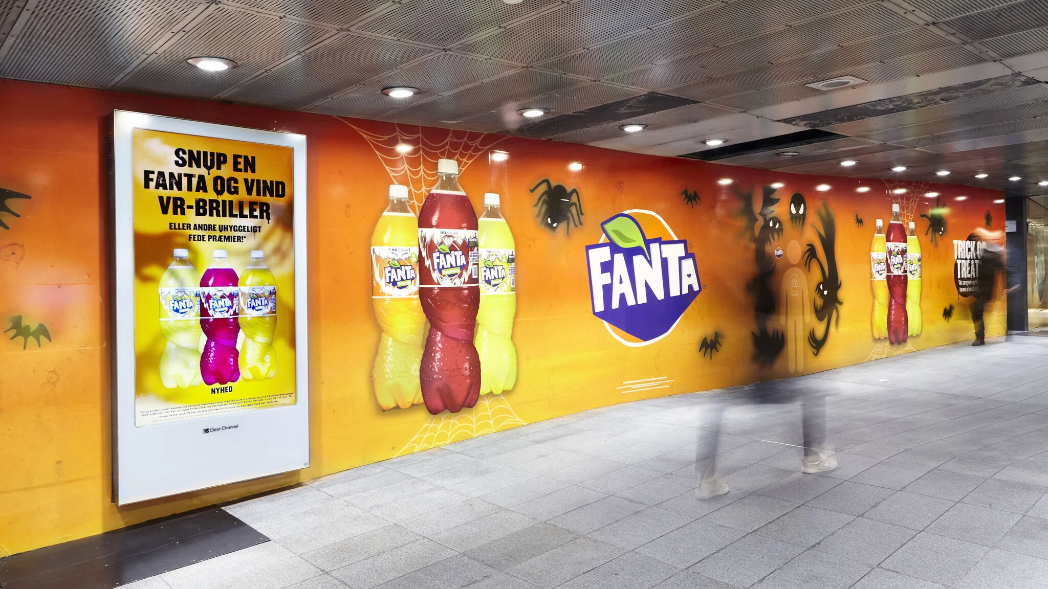 Orange Fanta Halloween wallpaper along a passage in Nørreport Station, with bottles, the Fanta logo, spiders, bats and a selfie spot surrounded by ghosts