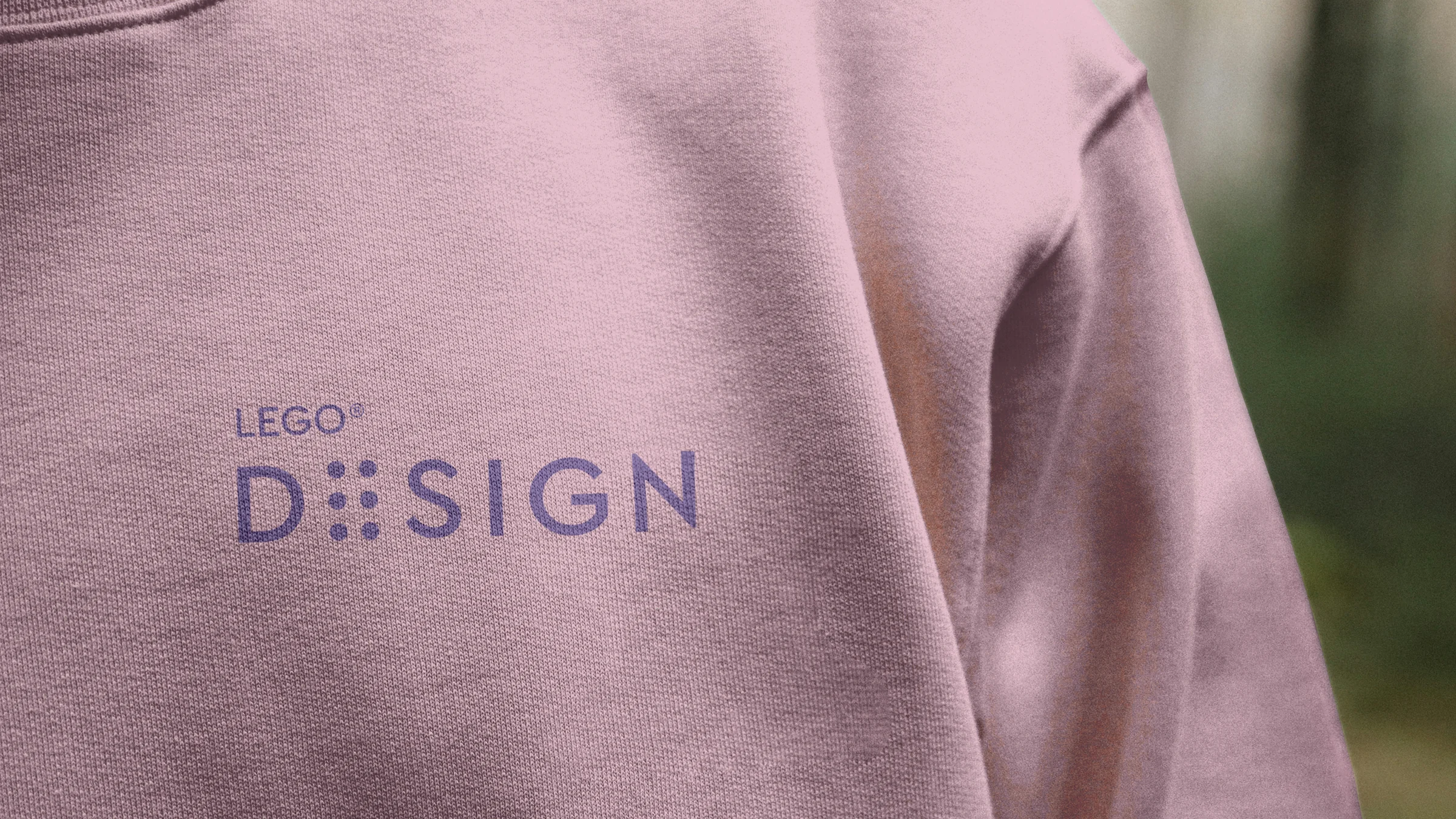 Close-up of a pink sweatshirt with the LEGO DESIGN logo printed in purple on the chest, the E made of six studs