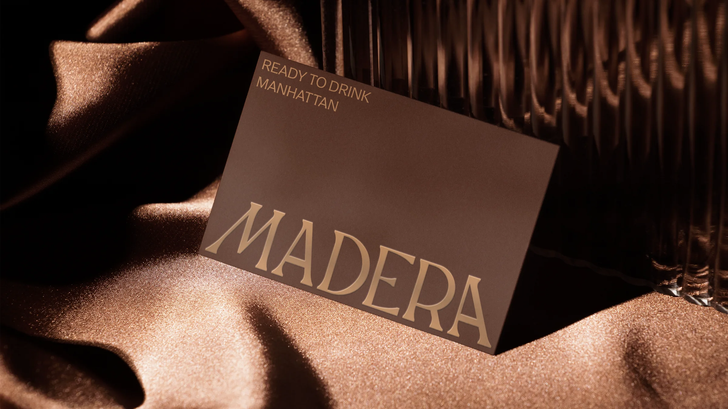 Madera card in copper lettering, Ready to drink Manhattan, resting on brown silk
