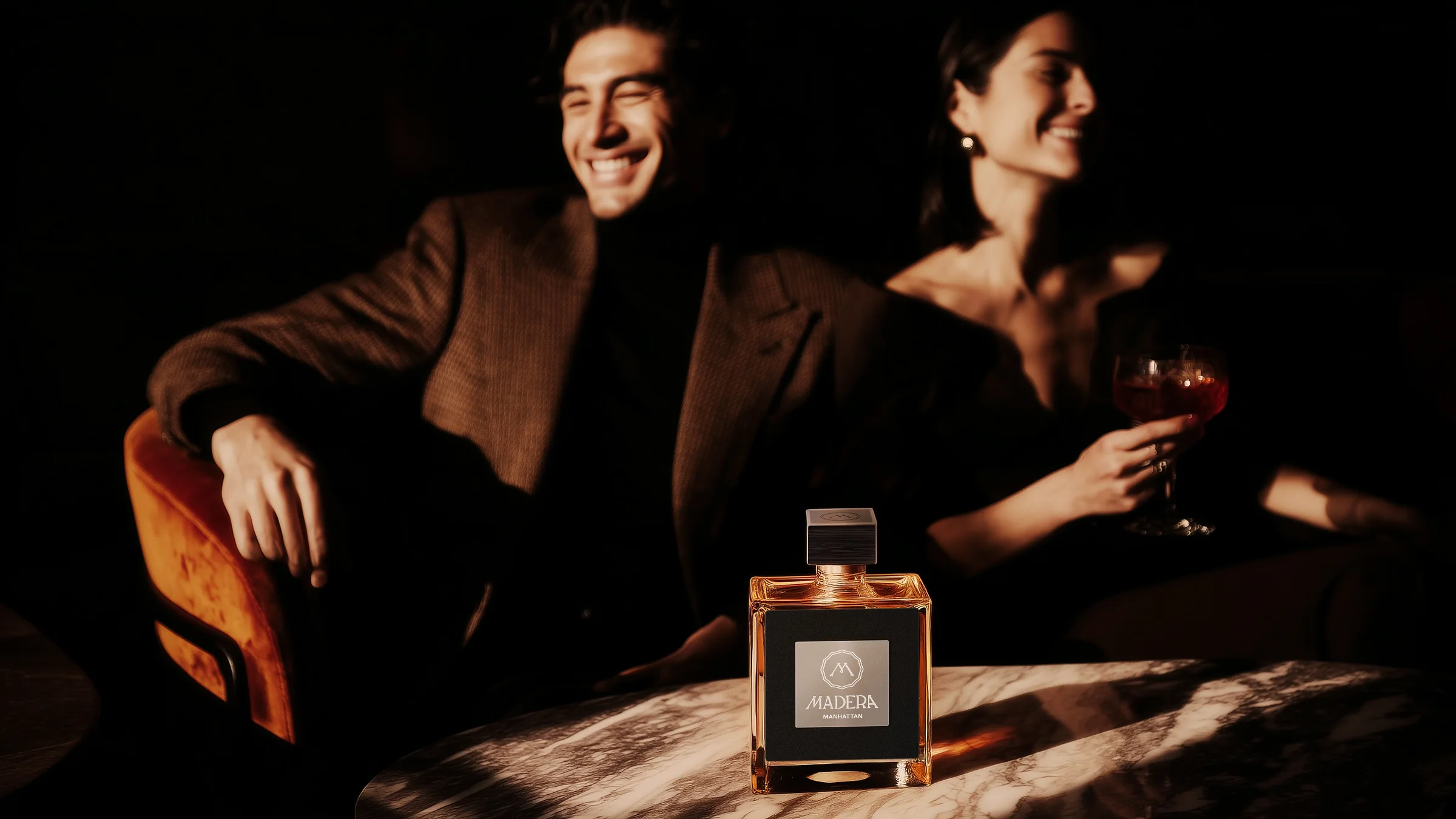 A couple laughing in a dark lounge with a bottle of Madera on a marble table